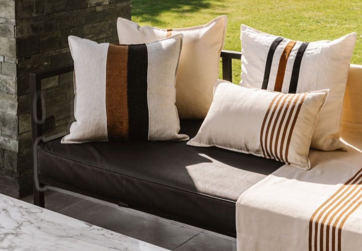 Almohadones de lino crudo con franjas suela y negras en un sillón exterior