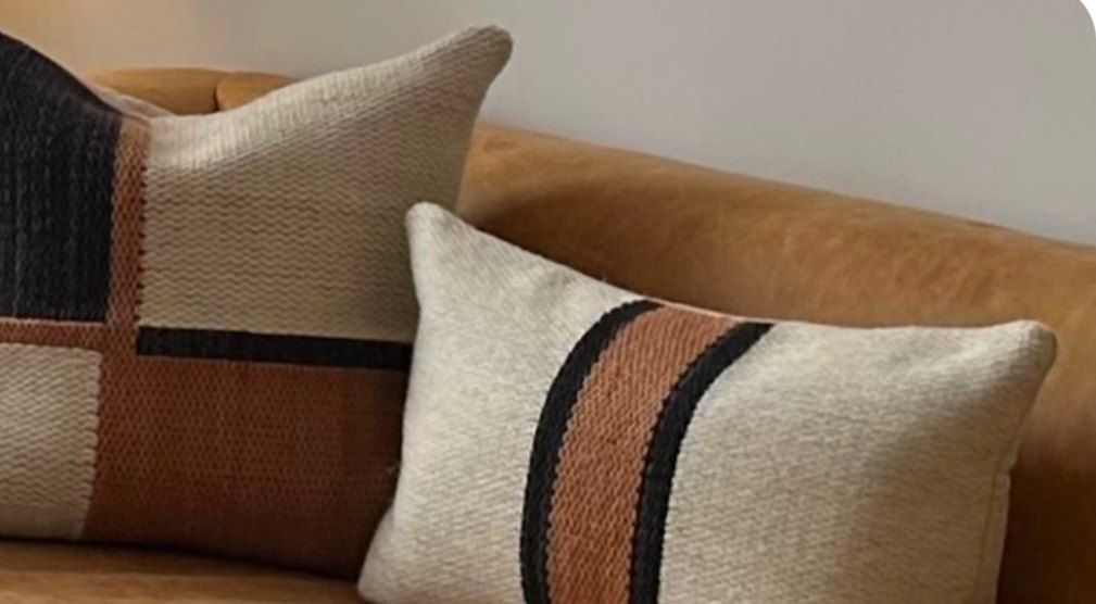 Almohadones tejidos en crudo, suela y negro sobre sillón de cuero
